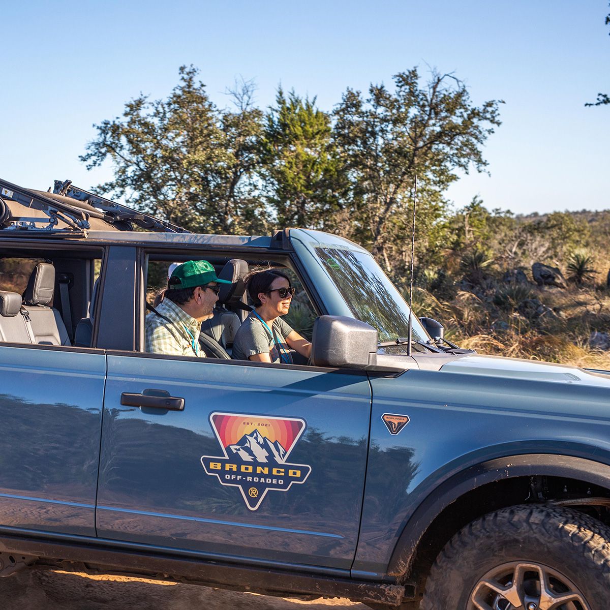 Man and woman sitting in blue bronco on the dirt trail.